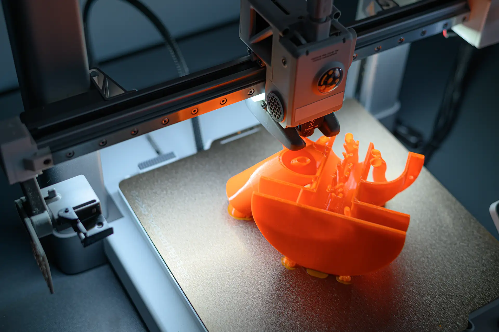 3D printer creating an intricate orange object showing complex geometry and fine detail capability