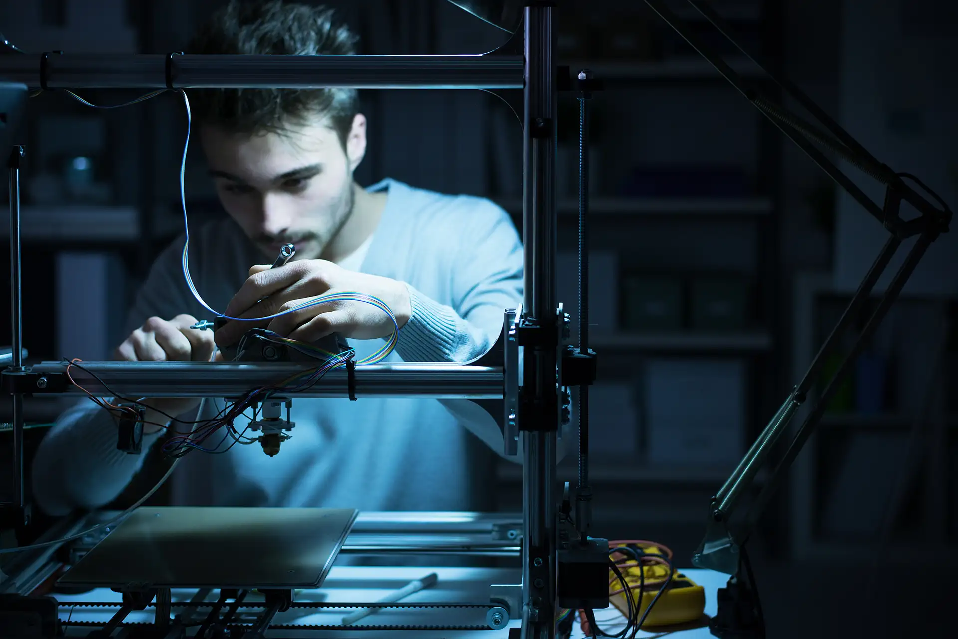 Man working on and operating a complex 3D printer in a workshop environment