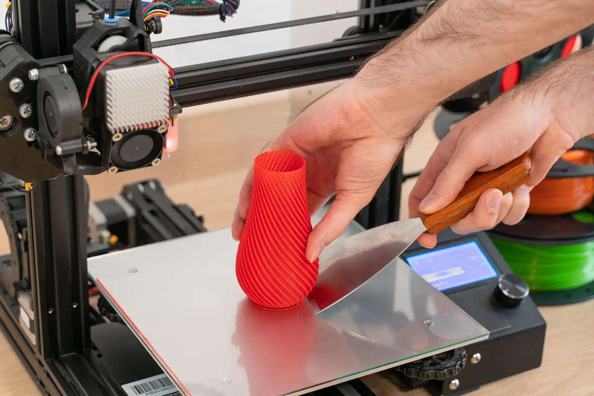 Person finishing and post-processing a 3D printed object with a tool at a workshop table