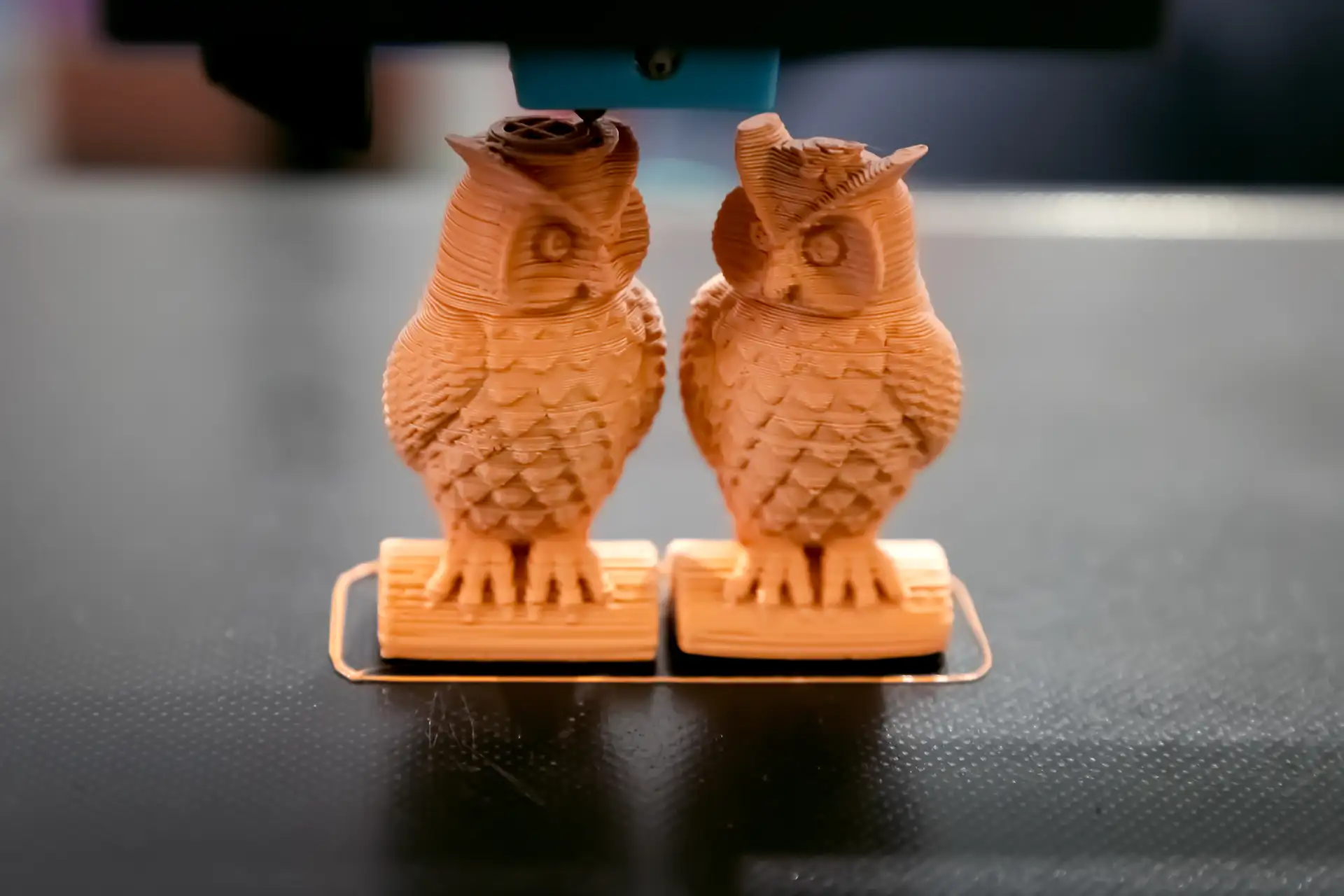 Two detailed 3D printed owl figurines sitting in a maker workspace