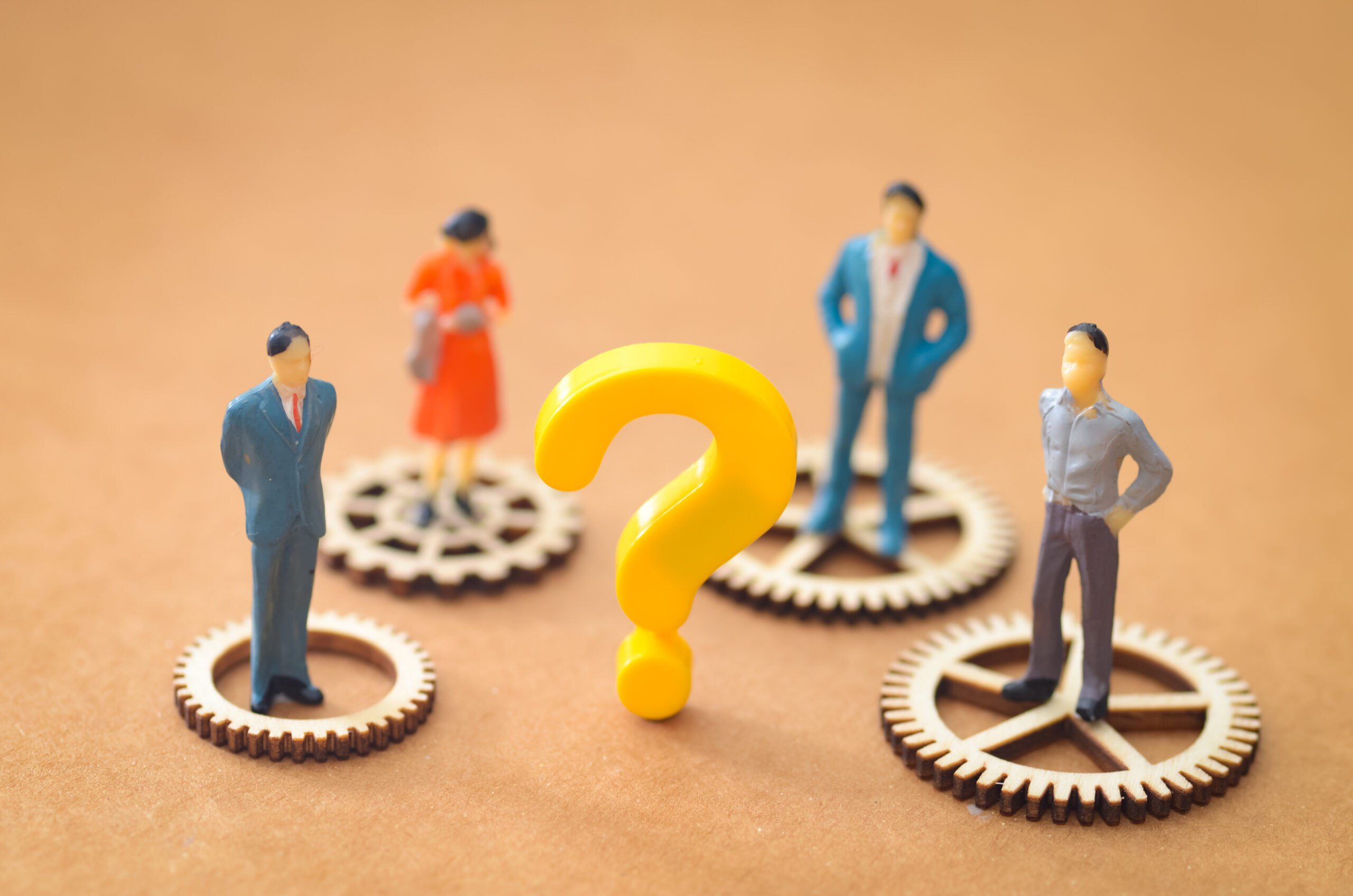 Uncertainty in Business: Miniature Figures Standing on Cogs Facing a Bright Yellow Challenge